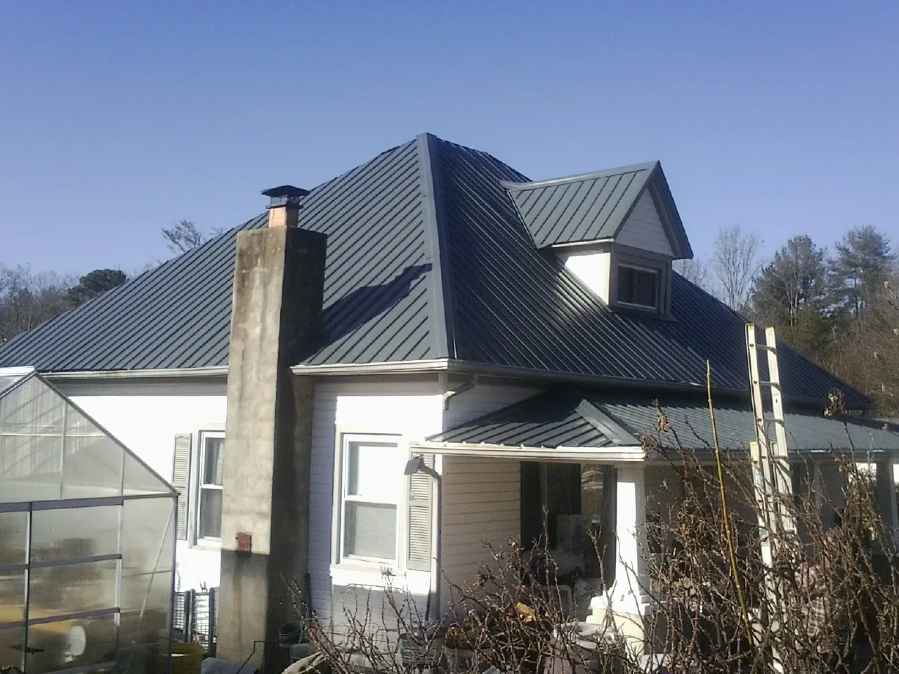 Dark blue standing seam metal roof on a white farmhouse with dormer — Slate & Tile Roof Repair by Roofing Brothers in Drakesboro