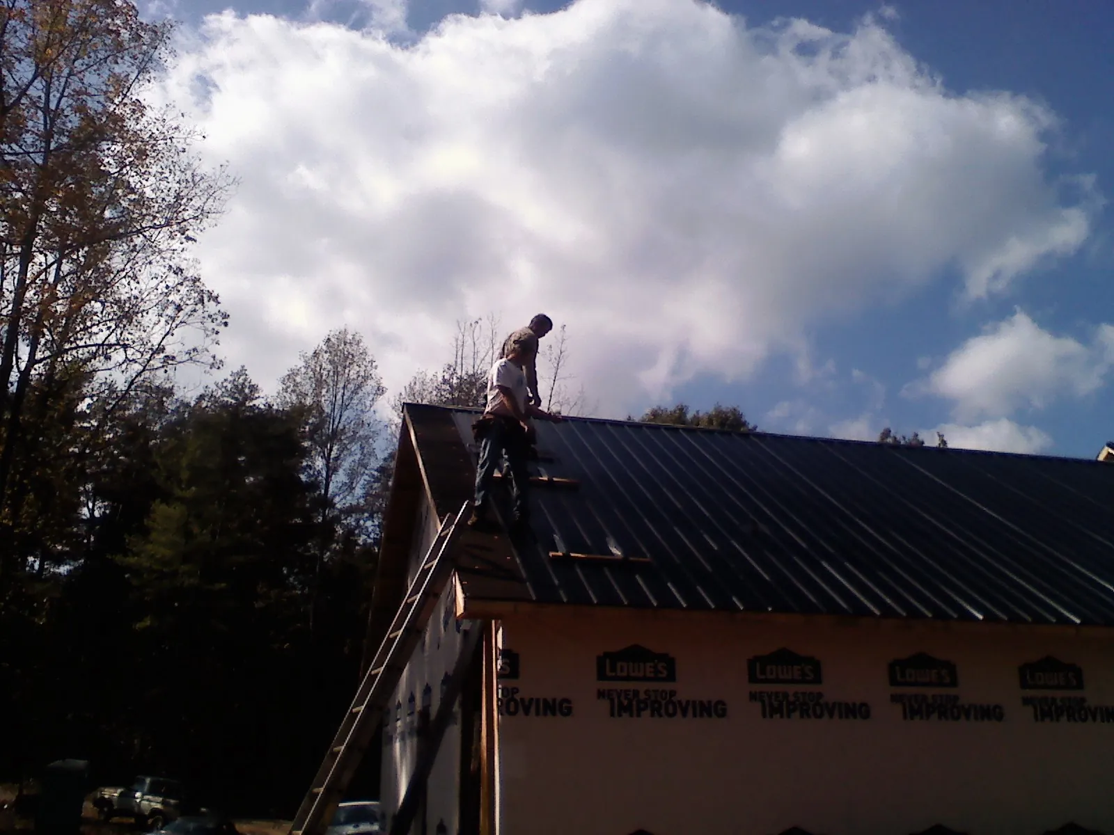 Roofer fastening dark metal panels high against a cloudy sky, from a Roof Inspection job in Drakesboro