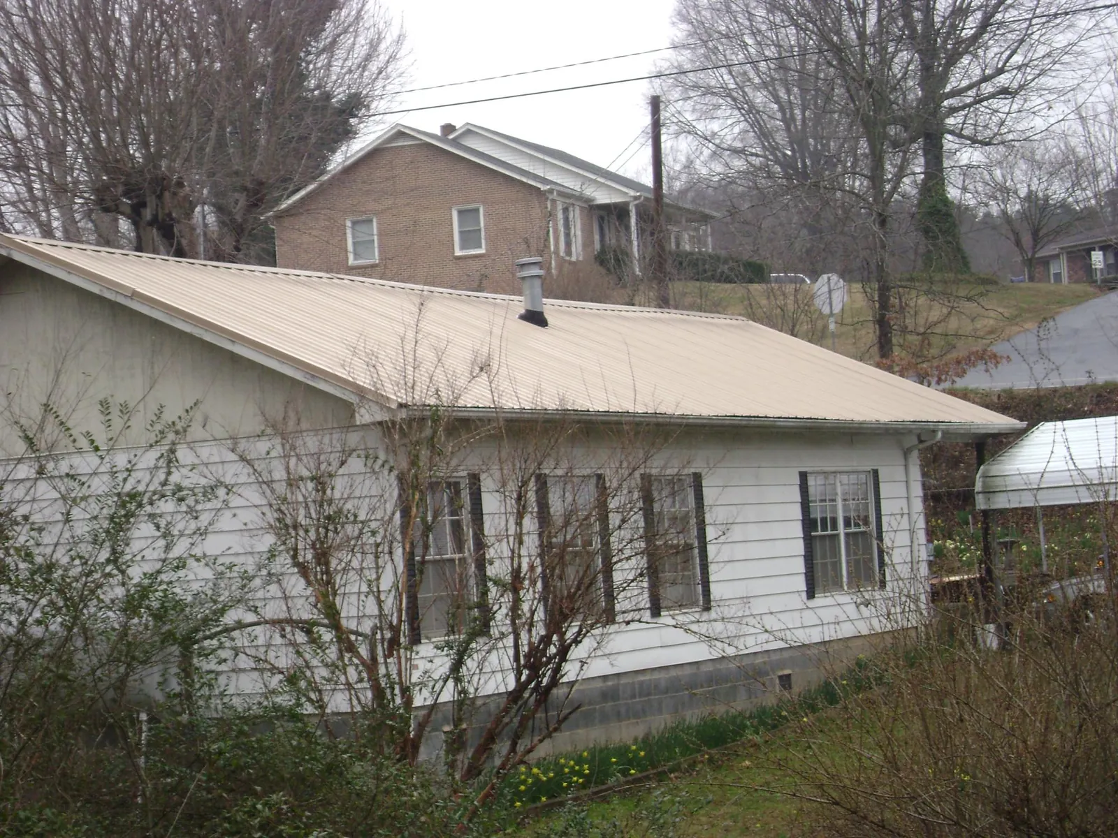 Tan metal roof on a white sided house set into a hillside — Commercial Roofing by Roofing Brothers in Drakesboro